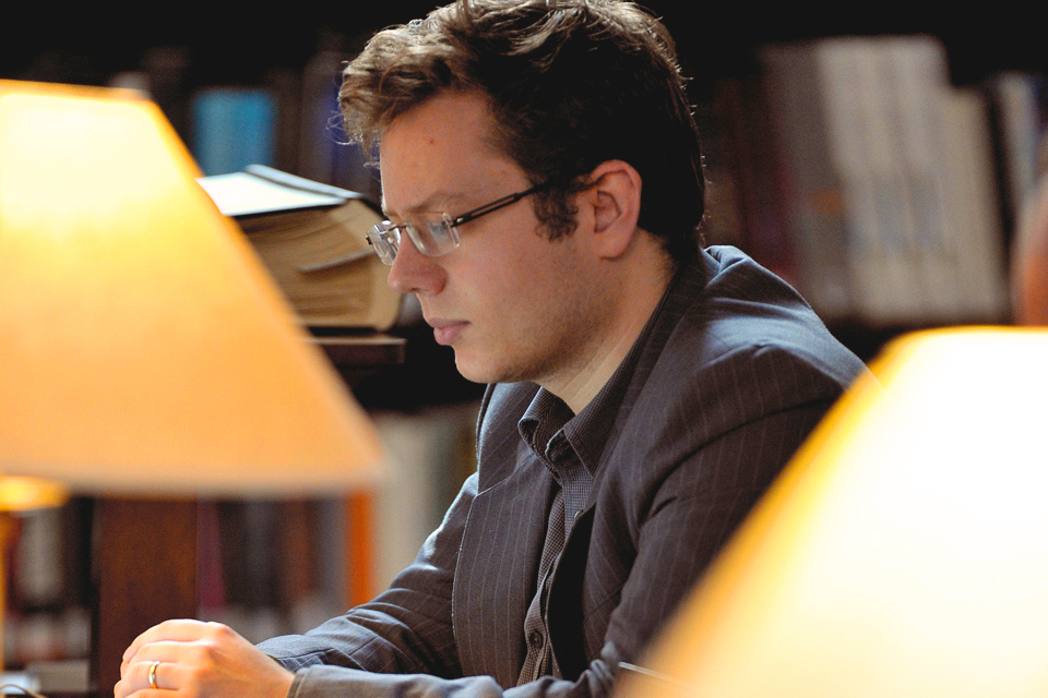 A male student, with glasses, studying in a library.